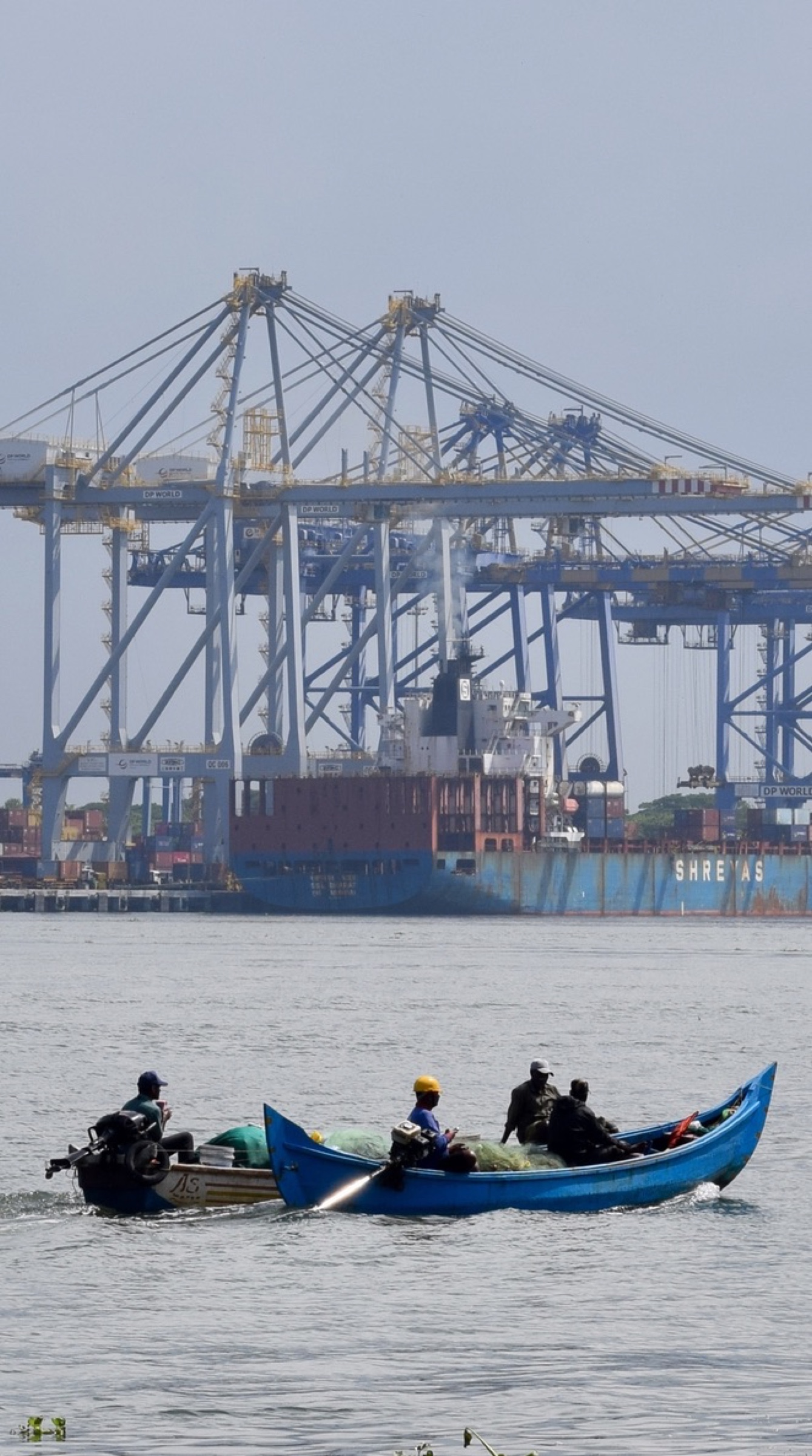 Fishermen crossing Kochi harbour in a blue boat with port cranes behind them